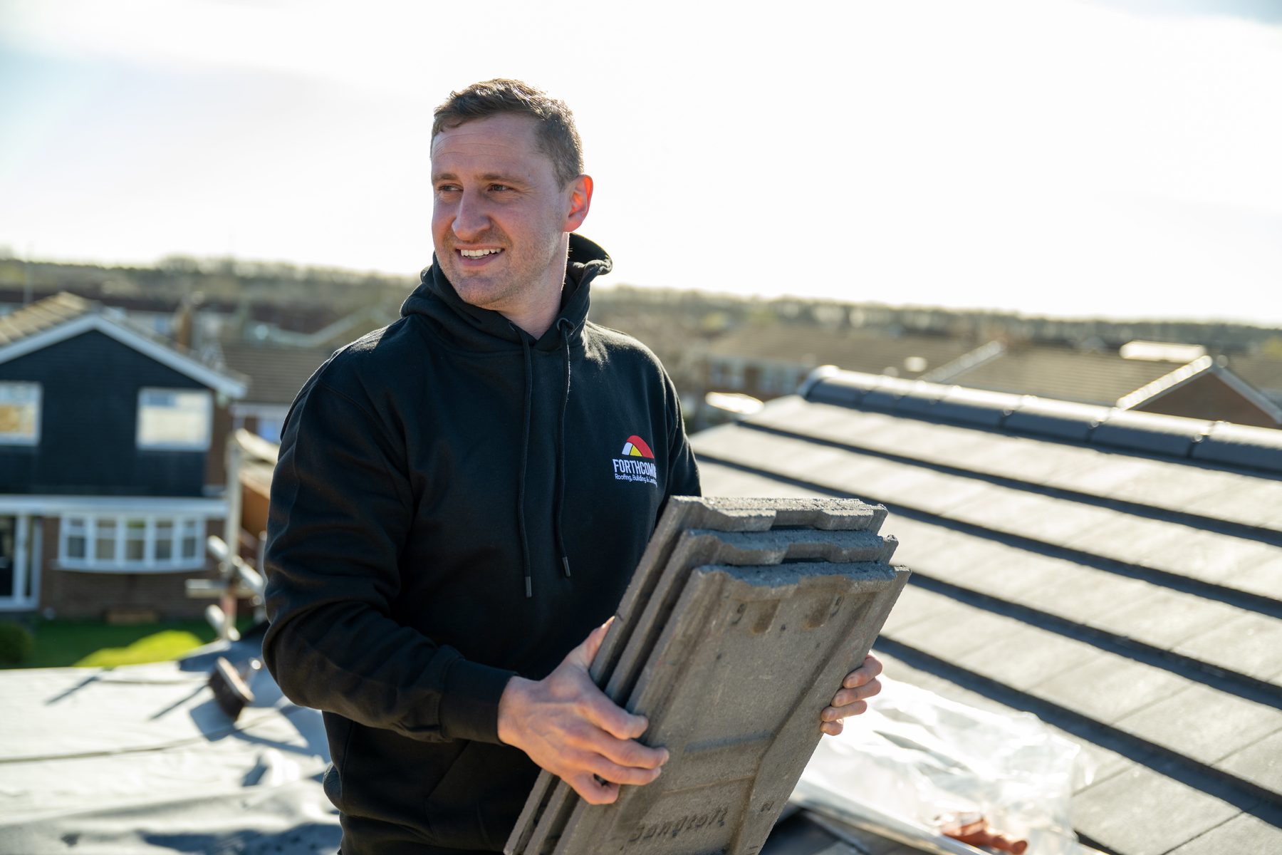 A roofer carrying tiles across a finished roof